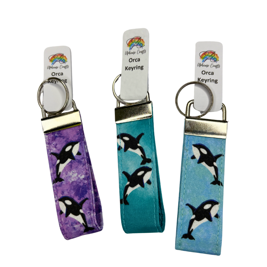 Three keychains with orca whale designs on a white background